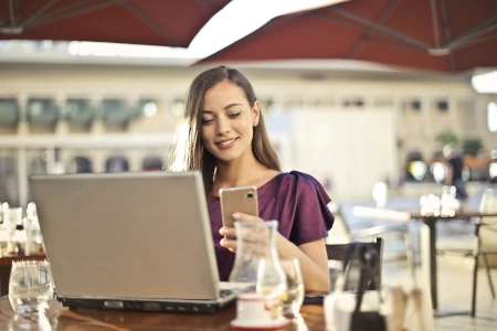 mulher jovem sorrindo com smartphone na mão e um laptop