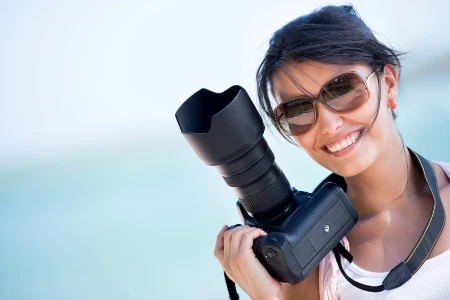 Fotógrafa sorrindo com câmera profissional nas mãos