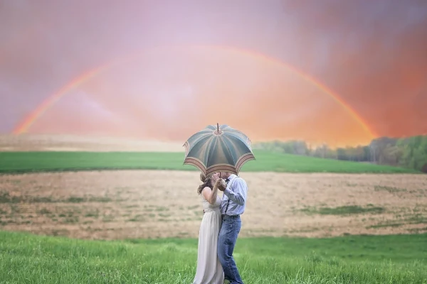 Casal com guarda-chuvas com arco-íris ao fundo