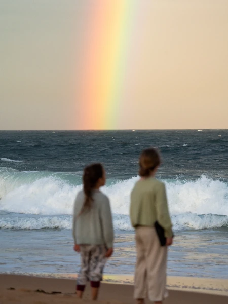 Crianças na praia observando um arco-íris